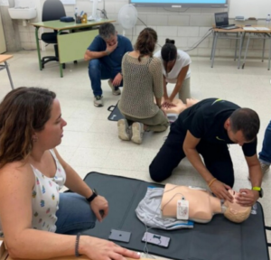 Grup d'empleats rebent formació en primers auxilis en una oficina, simulant una emergència amb un maniquí de RCP i un desfibril·lador DEA a prop.
